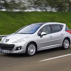 Srebrny Peugeot 207 1.6 HDI z czarnym dachem pędzi po drodze, za kierownicą siedzi mężczyzna, a obok niego pasażerka.