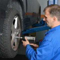 Mechanik w niebieskim kombinezonie dokręca koło kluczem pneumatycznym, dbając o to, z jaką siłą dokręcać koła.