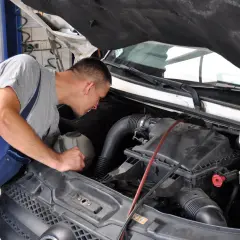 Mechanik w niebieskim ogrodniczkach pochyla się nad silnikiem, przygotowując się do wymiany świec żarowych.