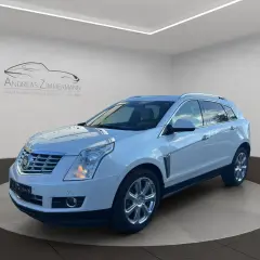 Biały Cadillac SRX z chromowanymi felgami, zaparkowany na obrotowej platformie w salonie samochodowym.