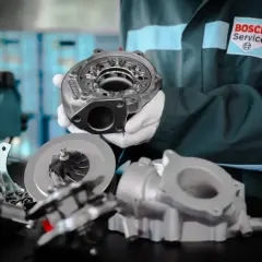 Mechanik w białych rękawiczkach prezentuje części turbosprężarki, sugerując domowe ustawienie sztangi turbiny.
