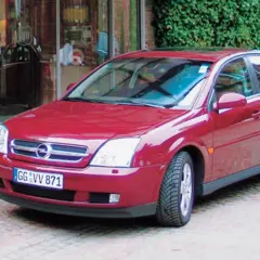 Czerwony Opel Vectra C GTS zaparkowany przed wejściem do hotelu.