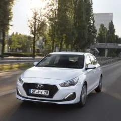 Biały Hyundai i30 1.4 benzyna na drodze. Kierowca w okularach przeciwsłonecznych. Opinie o tym modelu są pozytywne.