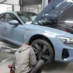 Mechanik pracuje przy podnośniku, wymieniając opony w szarym samochodzie elektrycznym. Szybka wymiana opon to klucz do bezpieczeństwa.