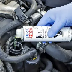 Ręka w niebieskiej rękawiczce wlewa płyn do płukania silnika Liqui Moly. Wiele osób szuka opinii o Ceratec, ale to właśnie ten produkt dba o czystość silnika.