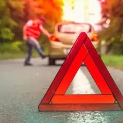 Trójkąt ostrzegawczy na drodze, gdzie nie można holować. Kierowca w kamizelce odblaskowej przy awaryjnym samochodzie.