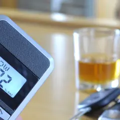 Alkomat z wyświetlaczem 0.02% BAC, szklanka z alkoholem i kluczyki samochodowe.