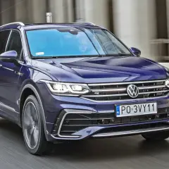Niebieski Volkswagen Tiguan w ruchu. Kierowca i pasażer widoczni przez przednią szybę. Wiele pozytywnych volkswagen tiguan opinie potwierdza jego wszechstronność.