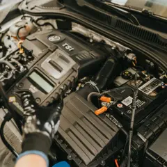 Mechanik w rękawiczkach sprawdza czujnik położenia wału za pomocą testera diagnostycznego podłączonego do akumulatora.