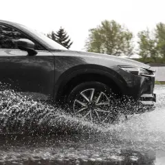 Ciemny samochód na mokrej drodze, koło rozpryskuje wodę, groźny aquaplaning.
