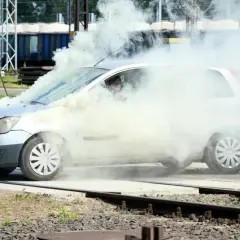 Srebrny Ford Fiesta z silnikiem diesla w obłokach dymu, na tle torów kolejowych.