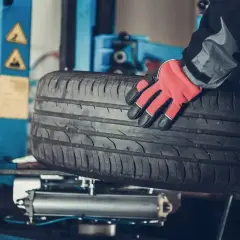 Mechanik w czerwonej rękawicy trzyma oponę. Czy można założyć opony 185 zamiast 195? Sprawdź w serwisie.