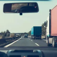 Widok z kabiny samochodu na drogę ekspresową z ciężarówkami i niebieskim kontenerem.