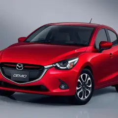 Czerwona Mazda Demio z błyszczącym lakierem i charakterystycznym grillem.