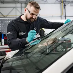Mechanik w okularach ochronnych i rękawiczkach naprawia szybę samochodową.