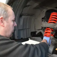 Mechanik w niebieskiej rękawiczce pracuje nad nowym, czerwonym, wylany amortyzator.