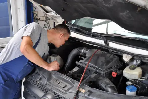 Mechanik w niebieskim ogrodniczkach pochyla się nad silnikiem, przygotowując się do wymiany świec żarowych.
