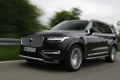 Czarne Volvo XC90 V8 pędzi po drodze, rozmazane drzewa i krajobraz świadczą o dużej prędkości.