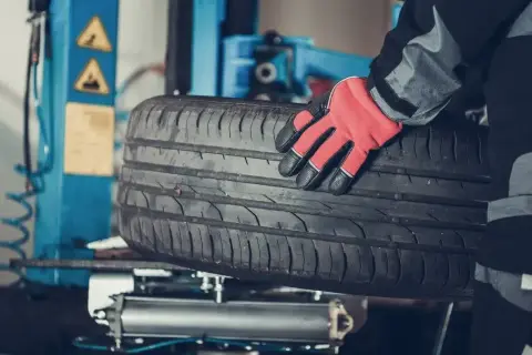 Mechanik w czerwonej rękawicy trzyma oponę. Czy można założyć opony 185 zamiast 195? Sprawdź w serwisie.