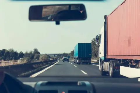 Widok z kabiny samochodu na drogę ekspresową z ciężarówkami i niebieskim kontenerem.