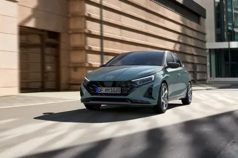 Nowoczesny Hyundai i20 w kolorze zielonym porusza się po miejskiej ulicy. To jeden z wielu stylowych modeli hyundaia.