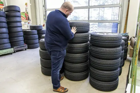 Mężczyzna wybiera najlepsze opony spośród wielu stosów. W magazynie panuje porządek, a opony są ułożone w równych rzędach.
