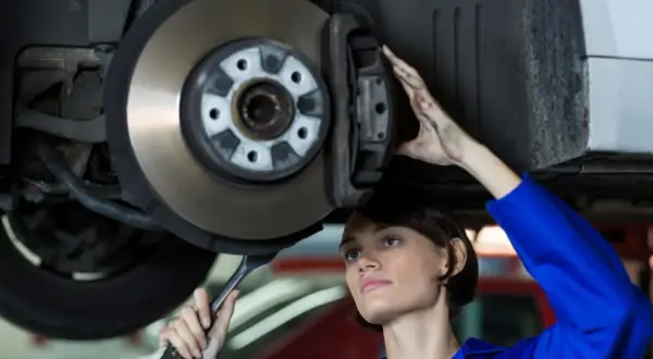 Mechaniczka w niebieskim kombinezonie wykonuje wymianę tarcz hamulcowych, trzymając klucz.