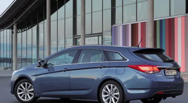 Niebieski Hyundai i40 kombi zaparkowany przed nowoczesnym budynkiem z kolorowymi pasami. Wiele osób chwali ten model, czytając **hyundai i40 opinie**.