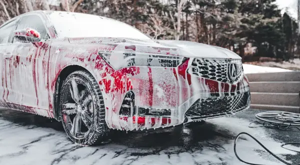Czerwony samochód pokryty pianą, stojący na śniegu. Czy można myć auto w mrozie? Piana spływa po karoserii, tworząc ciekawe wzory.