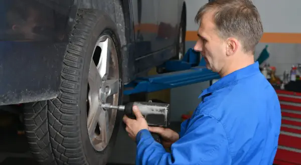 Mechanik w niebieskim kombinezonie dokręca koło kluczem pneumatycznym, dbając o to, z jaką siłą dokręcać koła.