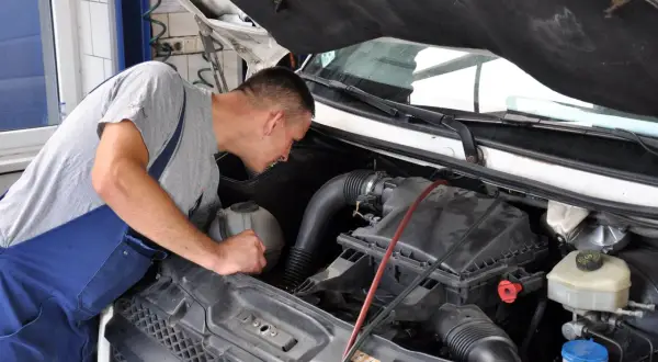 Mechanik w niebieskim ogrodniczkach pochyla się nad silnikiem, przygotowując się do wymiany świec żarowych.