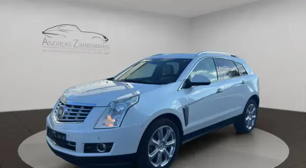 Biały Cadillac SRX z chromowanymi felgami, zaparkowany na obrotowej platformie w salonie samochodowym.
