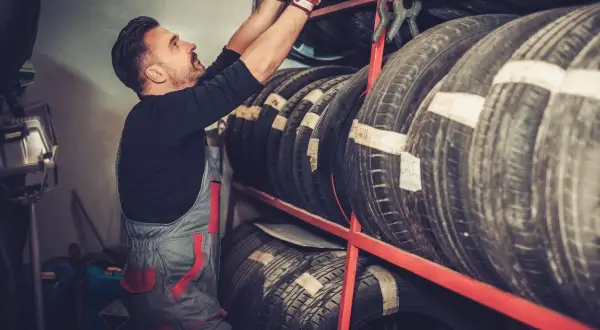 Mechanik w czerwonych rękawicach sięga po oponę Laufenn z regału.