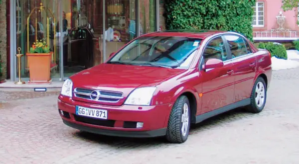 Czerwony Opel Vectra C GTS zaparkowany przed wejściem do hotelu.
