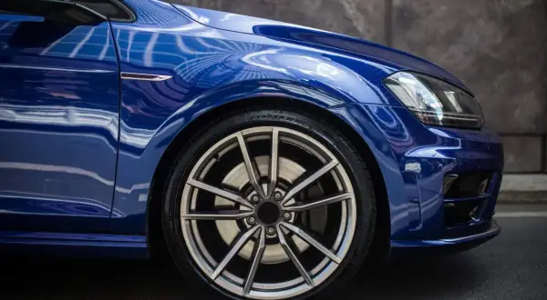 Błyszczące, niebieskie auto z felgami aluminiowymi. Widok z boku na przednie koło, idealny moment dokręcania kół aluminiowych.