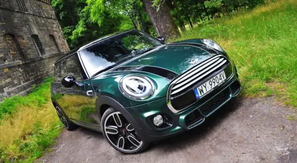 Zielony Mini Cooper na leśnej drodze. Wiele osób chwali sobie ten model, a jego opinie są zazwyczaj pozytywne.