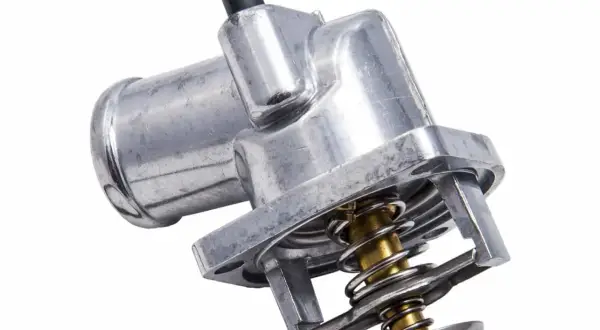 Metalowy termostat w samochodzie z widocznym mechanizmem sprężynowym i króćcem.