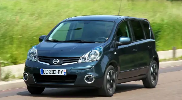 Ciemnozielony Nissan Note E11 w ruchu, z rozmytym tłem zieleni i drogi.