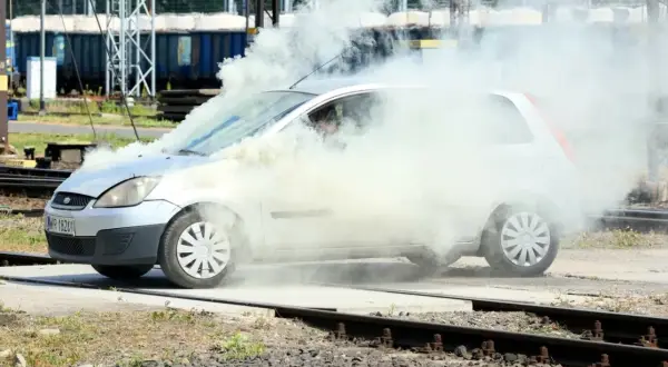 Srebrny Ford Fiesta z silnikiem diesla w obłokach dymu, na tle torów kolejowych.
