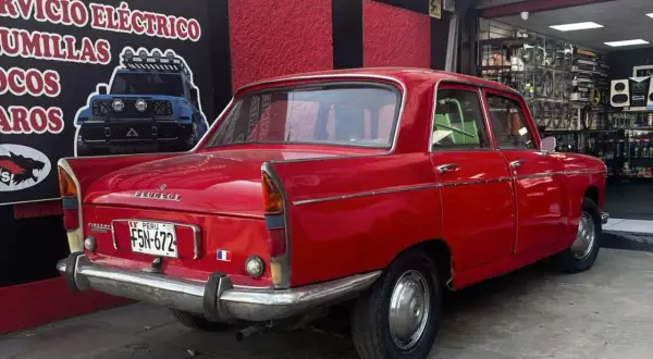 Czerwony Peugeot 404 z tablicą rejestracyjną z Peru, zaparkowany przed sklepem z częściami samochodowymi.