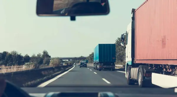 Widok z kabiny samochodu na drogę ekspresową z ciężarówkami i niebieskim kontenerem.