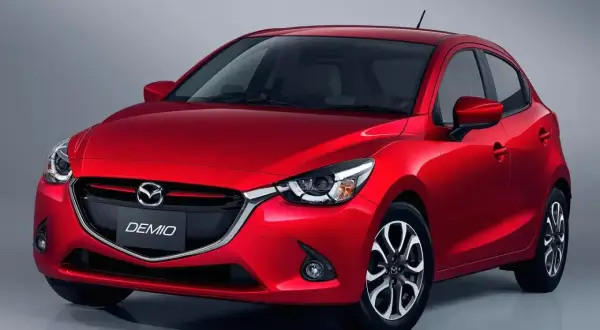 Czerwona Mazda Demio z błyszczącym lakierem i charakterystycznym grillem.