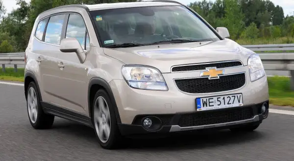 Złoty Chevrolet Orlando 1.8 benzyna na drodze. Rodzinny van w ruchu, z widocznym kierowcą.