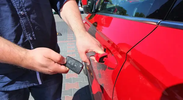Mężczyzna z kluczykiem w dłoni otwiera czerwony samochód, korzystając z systemu keyless go.
