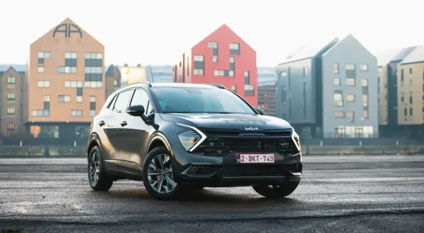 Czarny, mały SUV Kia Sportage stoi na mokrym asfalcie przed nowoczesnymi budynkami.