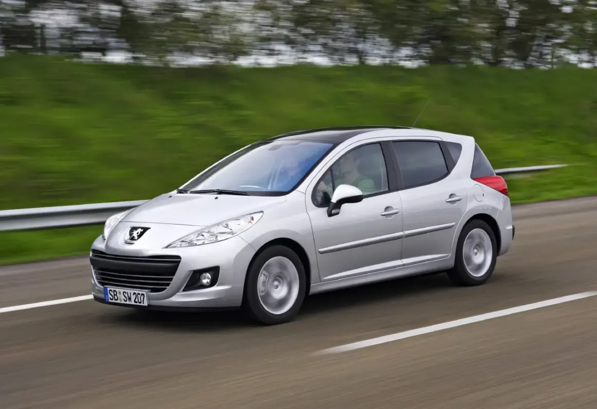 Srebrny Peugeot 207 1.6 HDI z czarnym dachem pędzi po drodze, za kierownicą siedzi mężczyzna, a obok niego pasażerka.