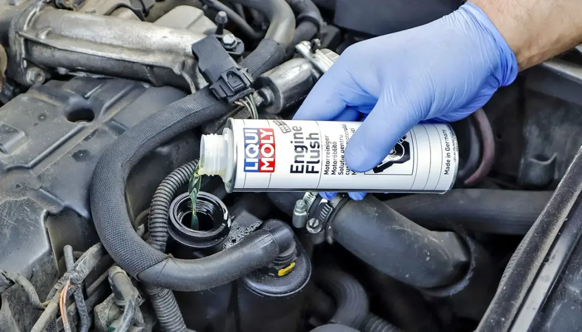 Ręka w niebieskiej rękawiczce wlewa płyn do płukania silnika Liqui Moly. Wiele osób szuka opinii o Ceratec, ale to właśnie ten produkt dba o czystość silnika.