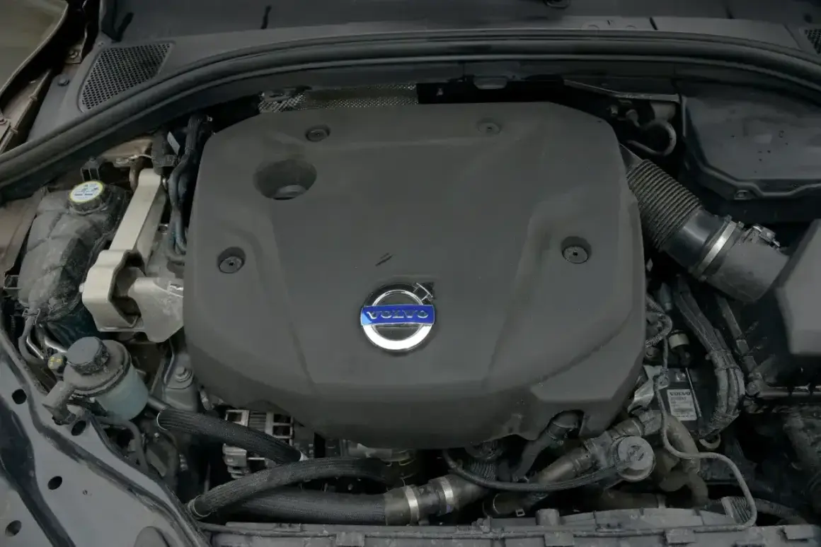 Silnik Volvo D4 pod czarną osłoną z niebieskim logo. Widoczne przewody i elementy układu chłodzenia.