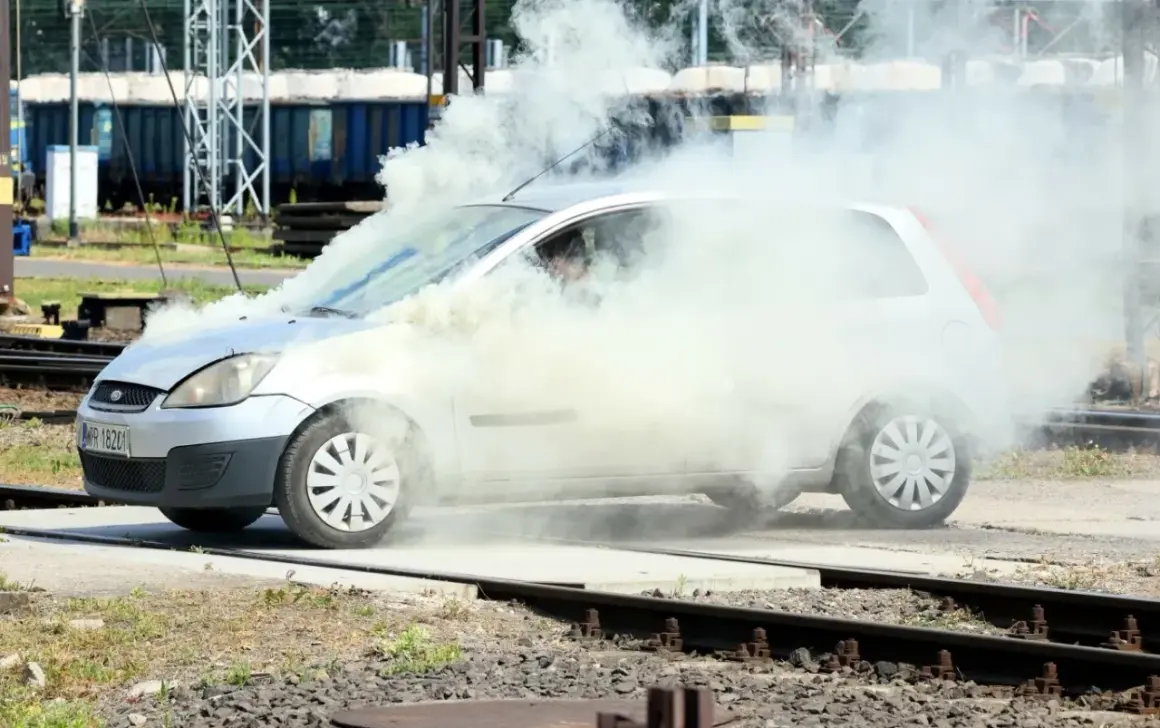Srebrny Ford Fiesta z silnikiem diesla w obłokach dymu, na tle torów kolejowych.