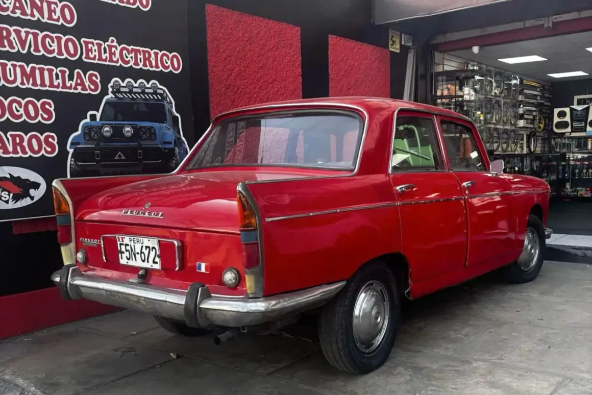 Czerwony Peugeot 404 z tablicą rejestracyjną z Peru, zaparkowany przed sklepem z częściami samochodowymi.